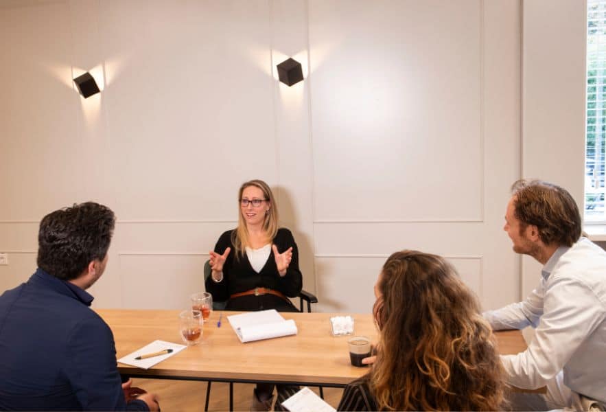 Esther Kroeze aan tafel in gesprek met gezinsleden. Luisterend naar elkaars verhaal. Ester helpt als therapeut en coach om met elkaar het gesprek aan te gaan.